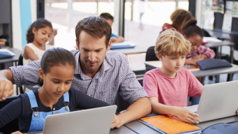 photo enseignant du primaire avec des élèves en classe travaillant sur ordinateur